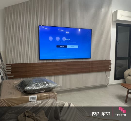 טלוויזיה מותקנת על קיר עם חיפוי עץ, חפצים מכוסים בניילון
